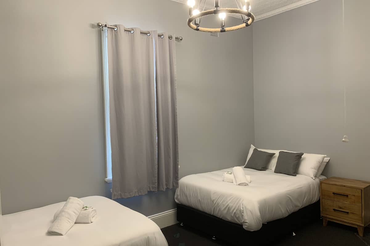 Un dormitorio con dos camas, una mesita de noche de madera, un candelabro y cortinas grises.