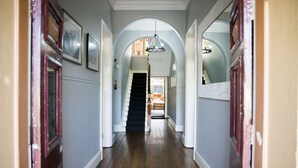 Un couloir doté d’un plancher en bois, de murs blancs et d’un escalier menant à une pièce comprenant un lit et une fenêtre.