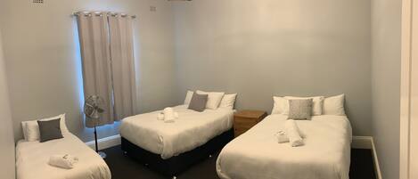 Quarto de hotel com três camas de solteiro, um ventilador de teto, uma mesa de cabeceira de madeira e um lustre.