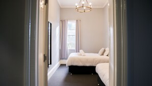 Une chambre avec deux lits, une grande fenêtre avec des rideaux et un lustre.