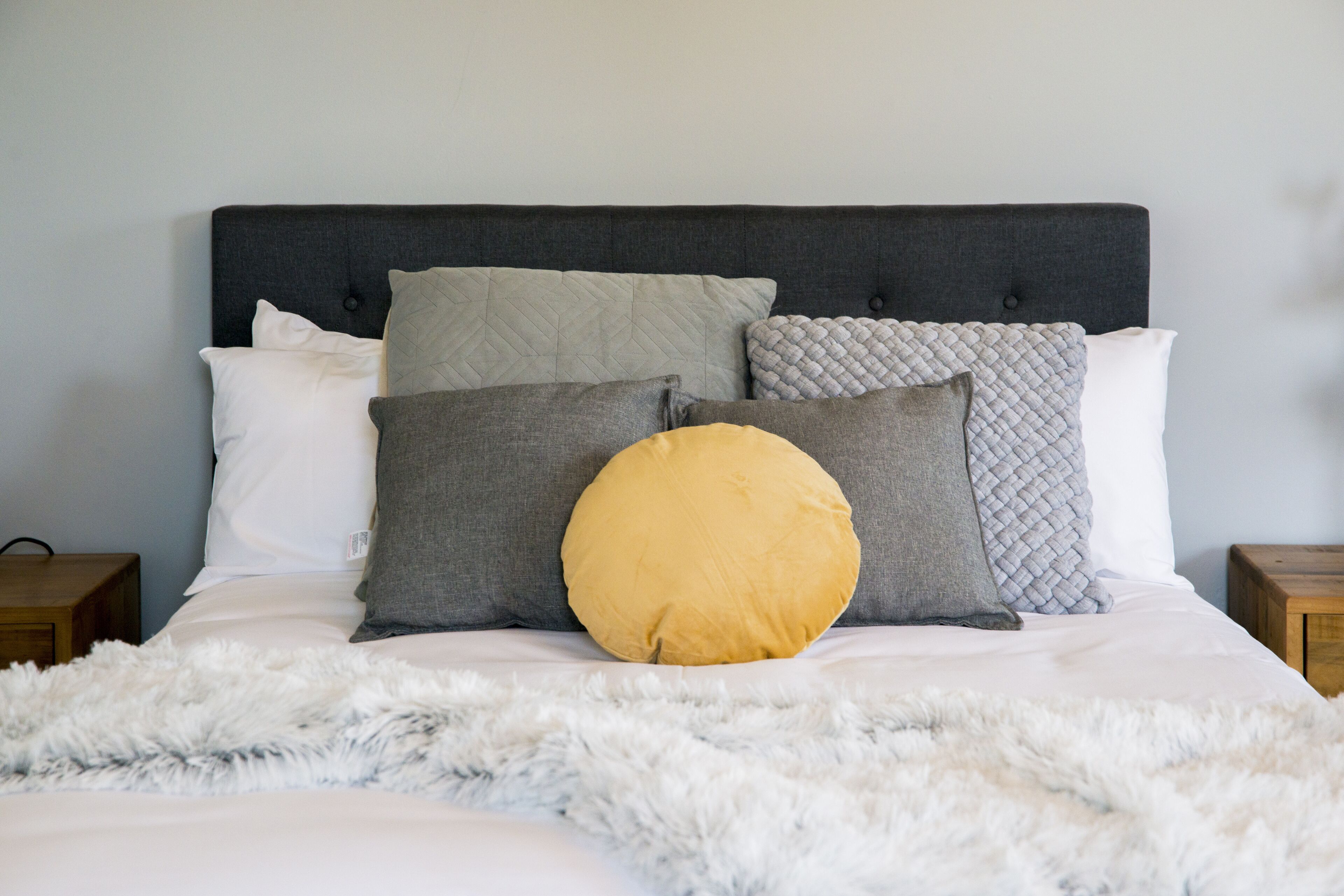 A neatly made bed with a fluffy white blanket and a variety of pillows in different shades and textures.