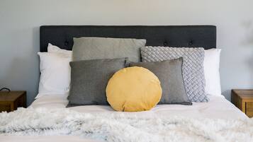 A neatly made bed with a fluffy white blanket and a variety of pillows in different shades and textures.
