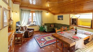 A cozy living room with a wooden ceiling, a green sofa, a dining table set for four, and a window with curtains. - BEAUTIFUL ATTIC ROOM WITH A VIEW OF THE SKI SLOPES (BORMIO)