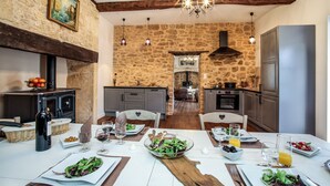 A rustic dining area with stone walls, wooden beams, and a chandelier. There is a table set with plates, glasses, and a bottle of wine. - BISE stylish 1600 SF wifi (Vitrac)