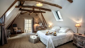 A cozy attic bedroom with a sloped ceiling, a large bed with a white quilt, a wooden dresser, and a small window. - BISE stylish 1600 SF wifi (Vitrac)