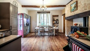 A kitchen with wooden flooring, a dining table with chairs, a refrigerator, a microwave, and a stone wall with a painting. - BISE stylish 1600 SF wifi (Vitrac)