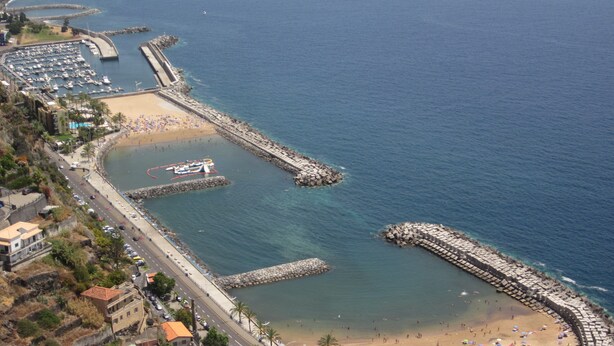 An aerial view of a coastal area with a marina, beach, and rocky breakwaters. - CASA IVA 3 bedroom, 3 bathroom House with swimming pool and sea views (Estreito da Calheta)