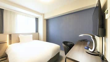 Habitación de hotel con una cama grande, un escritorio con computadora y lámpara, un televisor montado en la pared y una ventana con cortinas.
