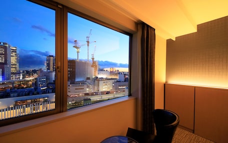 Habitación de hotel con un ventanal grande que ofrece vistas a un paisaje urbano, incluyendo edificios y una obra en construcción.