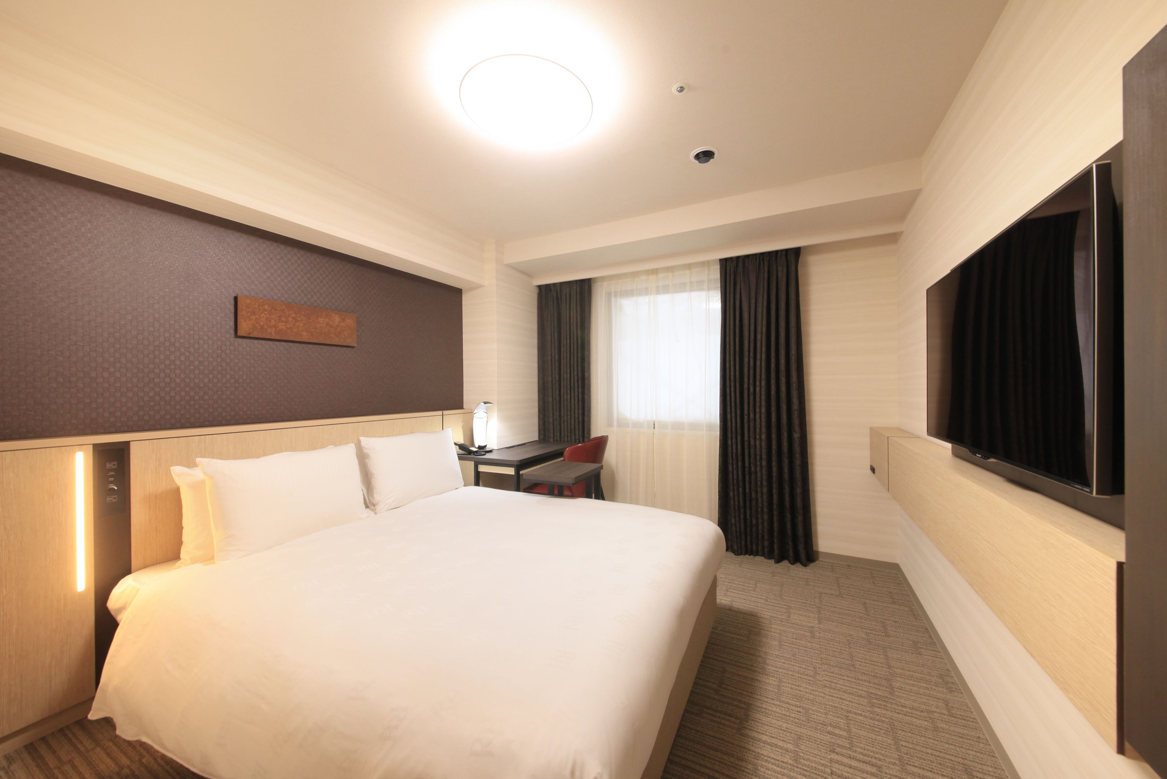 A hotel room with a large bed, a desk, a chair, a television, and a window with curtains.