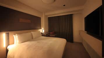 Una habitación de hotel con una cama grande, un escritorio con silla, televisor y una ventana con cortinas.