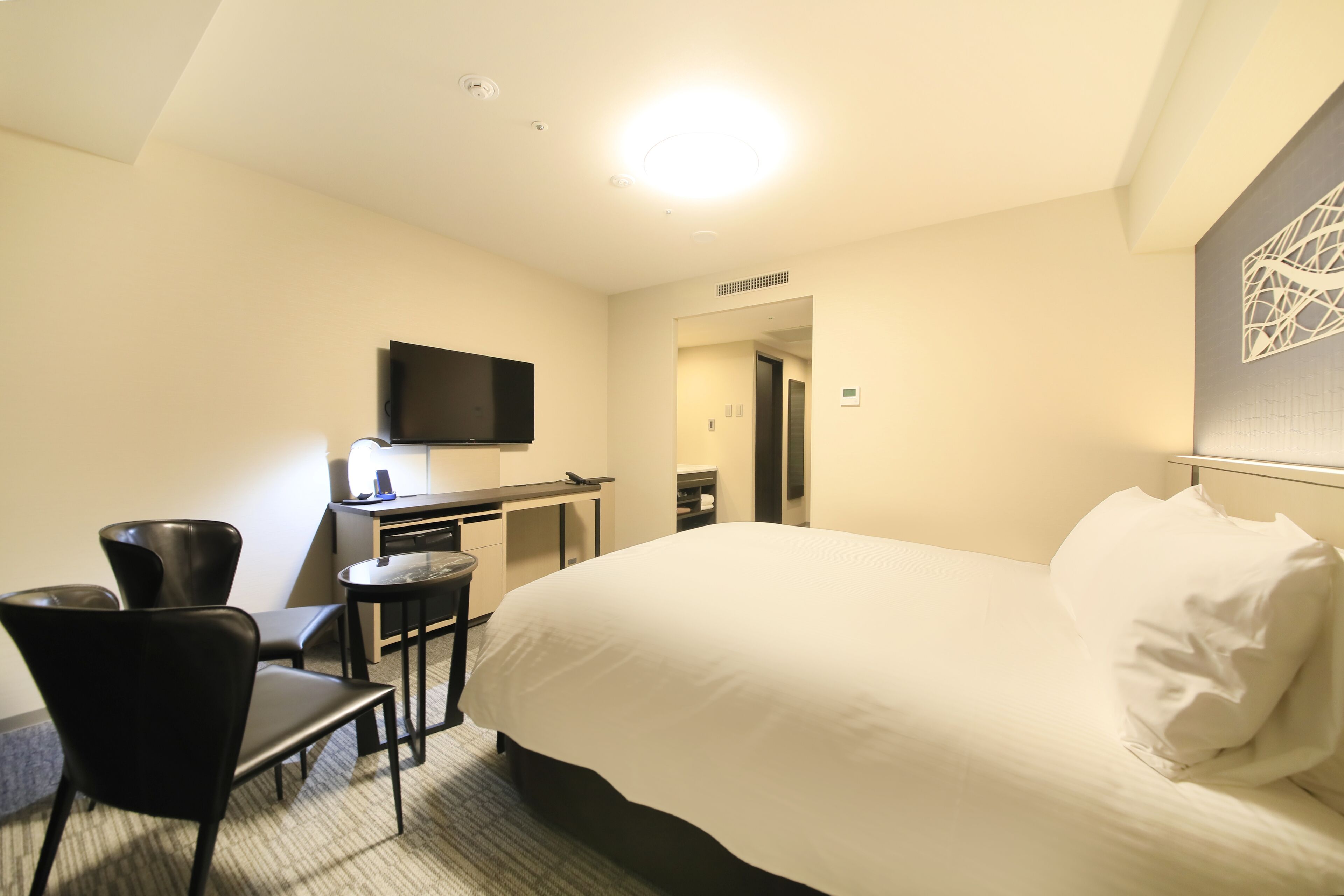 A hotel room with a bed, a desk, a chair, a television, and a small table.