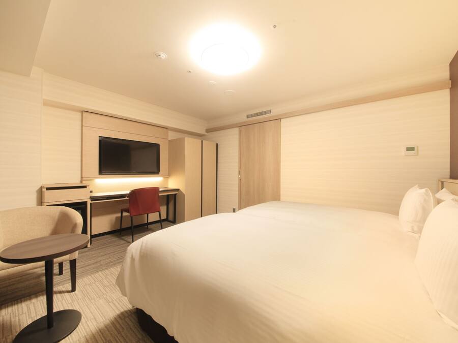 A hotel room with a large bed, a desk with a chair, a television, and a wardrobe.