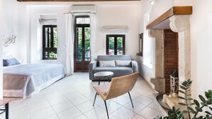 Amplia habitación con cama, sofá, sillón de mimbre, mesita y chimenea.