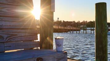 A wooden dock with a bench and a cup, overlooking a body of water with a pier in the background.