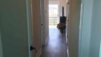 Un couloir avec un plancher en bois, des murs blancs et une porte sur le côté gauche.