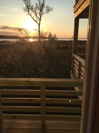 Una terraza de madera con vista a una puesta de sol sobre el agua, rodeada de césped y árboles.
