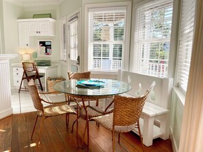 A dining area with a glass-top table surrounded by wicker chairs, white cabinetry, and windows with blinds. - Spacious House, 1 Back, Beach Access, Big Porches, Inlet Views, Pretty Sunsets! (Tybee Island)