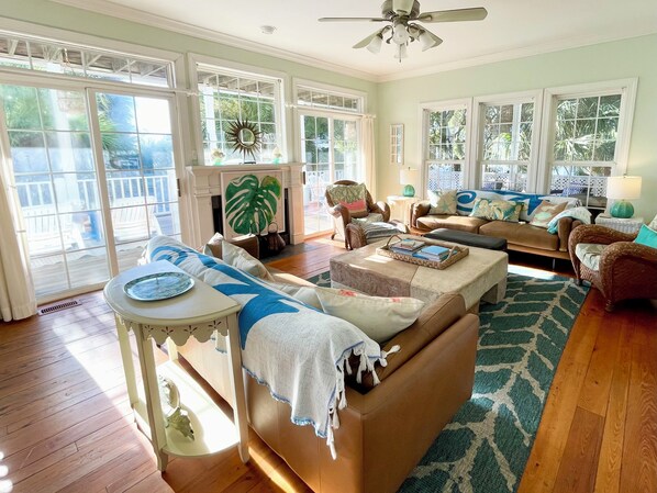A spacious living room with a large window, a ceiling fan, and a fireplace. - Spacious House, 1 Back, Beach Access, Big Porches, Inlet Views, Pretty Sunsets! (Tybee Island)