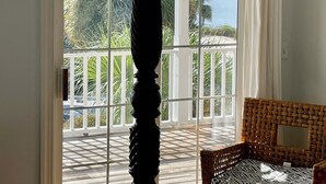 Une chambre dotée d’un lit à baldaquin, d’un fauteuil en osier et d’une grande porte-fenêtre coulissante donnant sur un balcon avec vue sur la mer et la végétation.