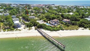 Vue aérienne d’une zone résidentielle côtière, avec des maisons, une plage et une jetée qui s’avance dans l’eau.