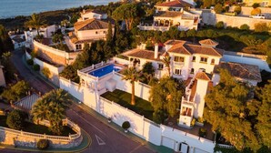 A coastal residential area with houses featuring Mediterranean architecture, a swimming pool, and a curved road.