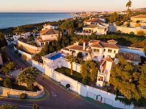 A coastal residential area with houses featuring Mediterranean architecture, a swimming pool, and a curved road.