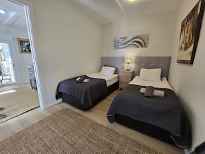 A hotel room with two beds, a nightstand, a lamp, and a painting on the wall.