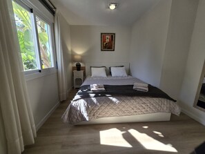 A bedroom with a bed, a nightstand, a lamp, and a window with curtains.
