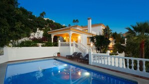 Un área de piscina con una cerca blanca, sillas de descanso y una escalera que lleva a una casa con balcón.