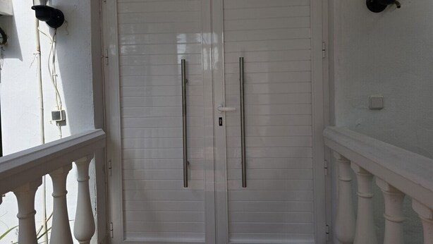 Una puerta blanca con dos manijas, una barandilla blanca y un aplique fijado a la pared.