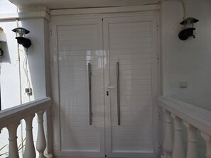 A white door with two handles, a white railing, and a wall-mounted light fixture.