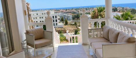 A balcony with a view of the sea, furnished with two sofas and a table.