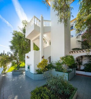 A modern building with a white facade, multiple balconies, and lush greenery.
