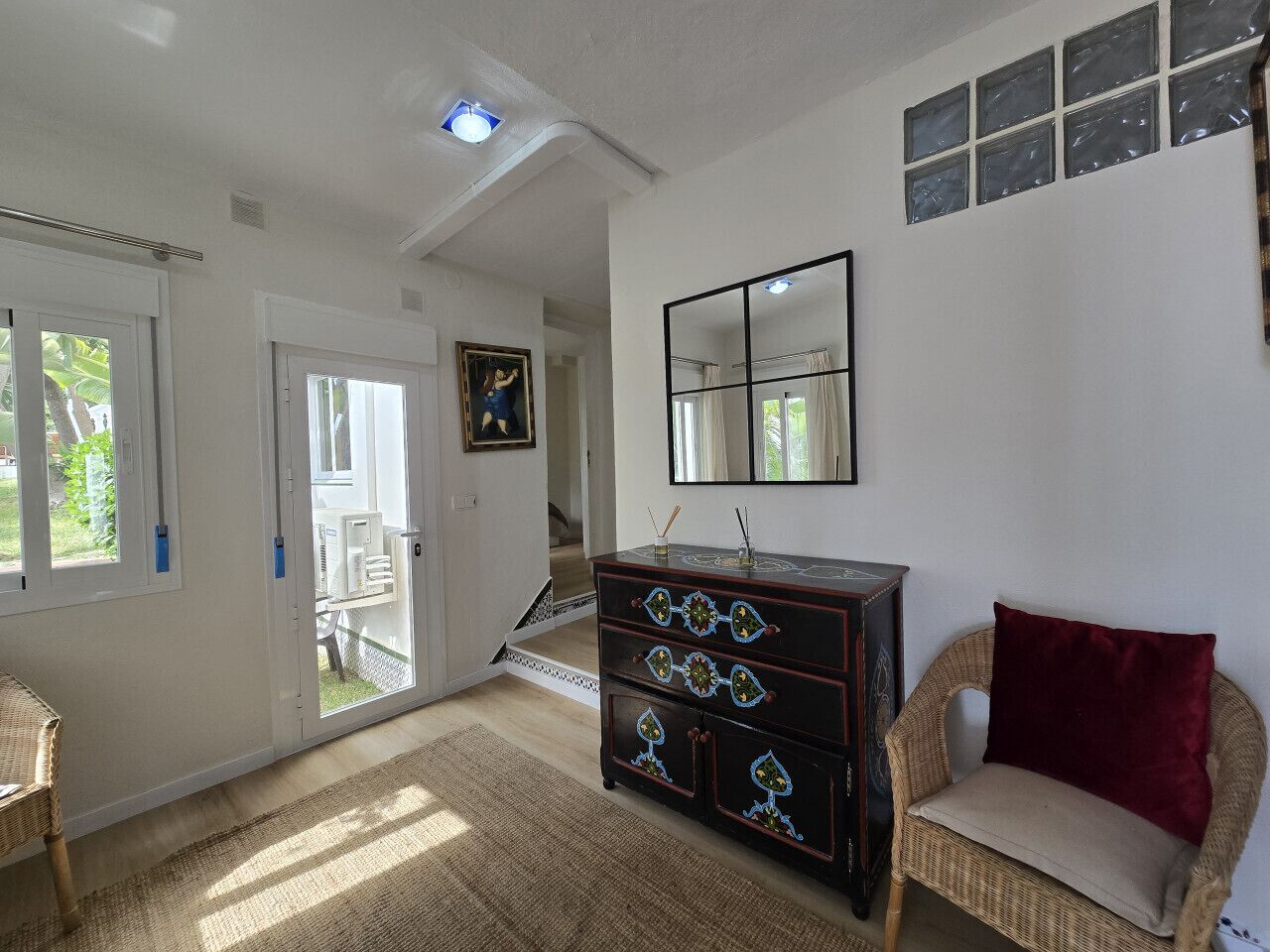 Et værelse med en stor trækommode, en fletstol, et spejl og en dør til en balkon.