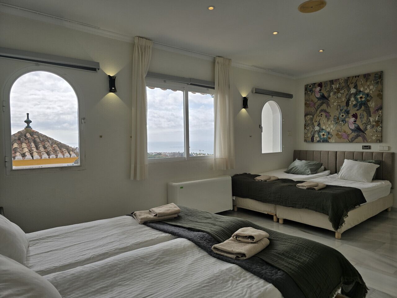 Un dormitorio moderno con dos camas, ventanas amplias y vistas a la ciudad.