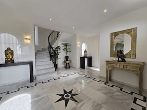 Ein geräumiges Foyer mit Marmorboden, einer Treppe und einem Konsolentisch mit dekorativem Spiegel.