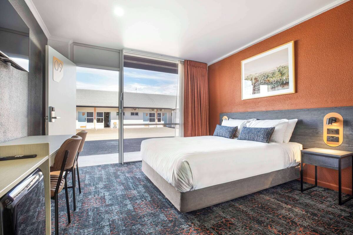 A hotel room with a bed, desk, chairs, and a view of the outside.