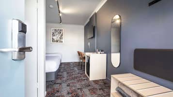 Una habitación de hotel moderna con una cama, un escritorio y una silla, un espejo grande y un cuadro en la pared.
