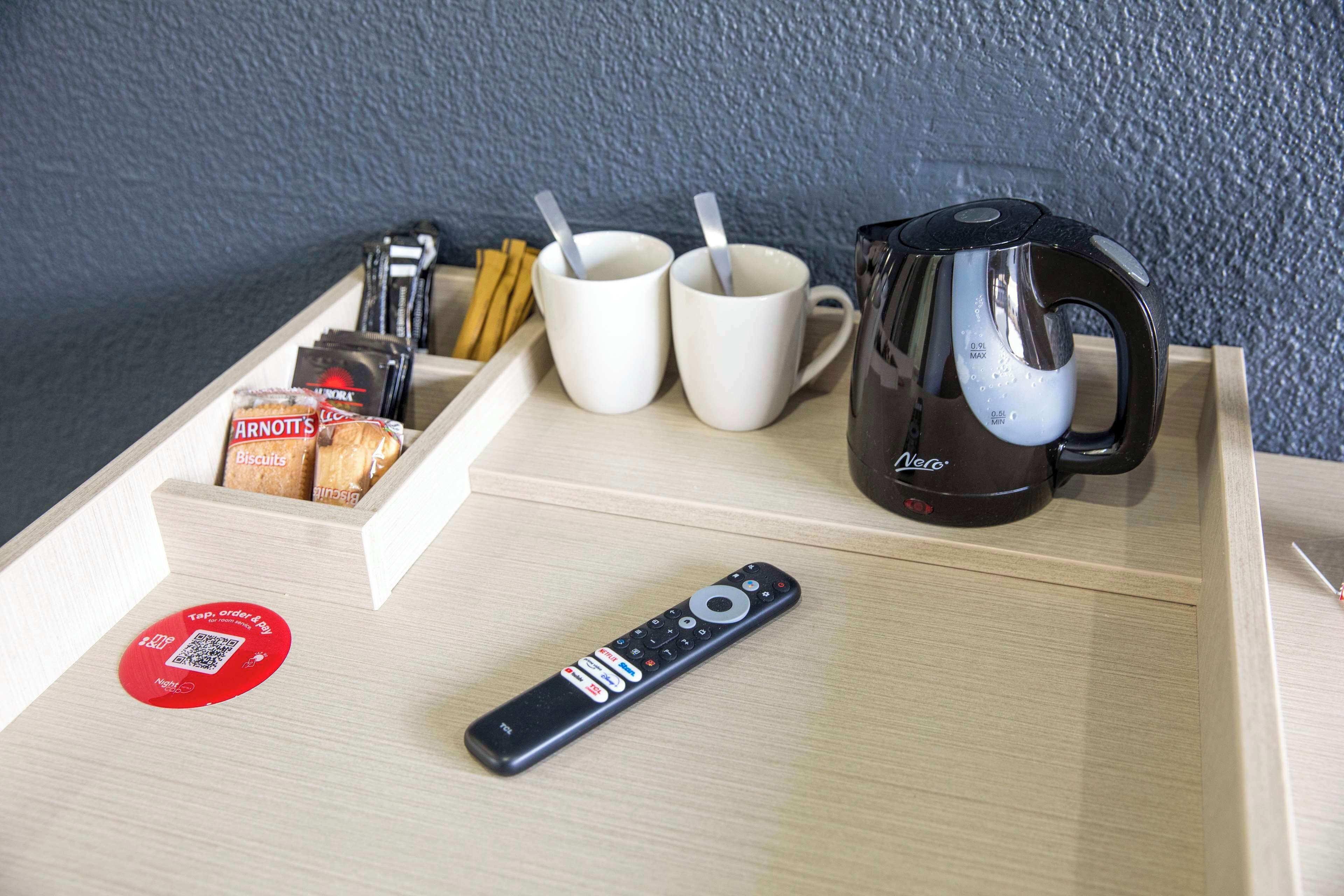 Un plateau avec une télécommande, deux tasses, des biscuits et une bouilloire.