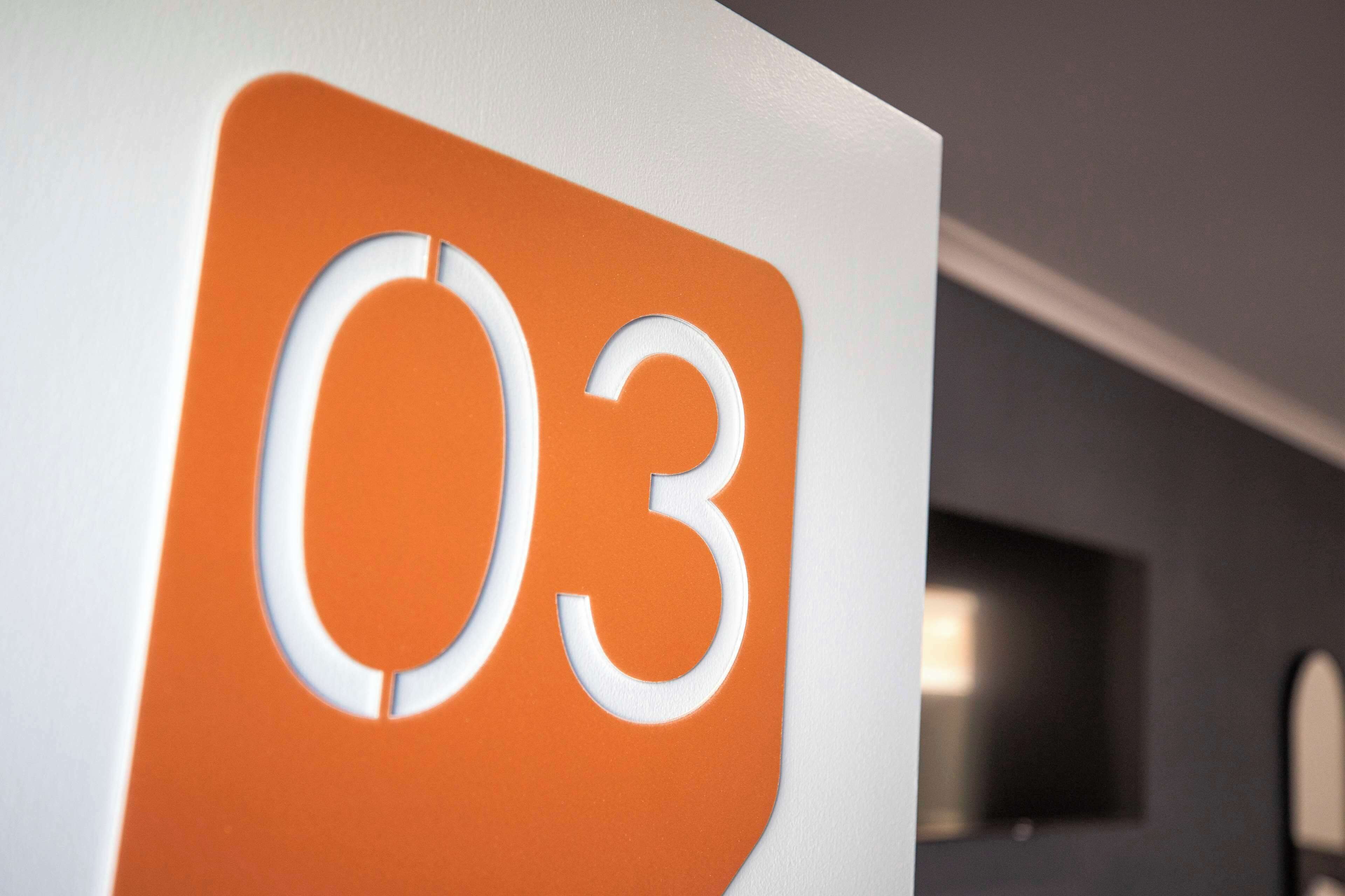 Nærbillede af et skilt med nummeret '03' i hvid skrift på orange baggrund.