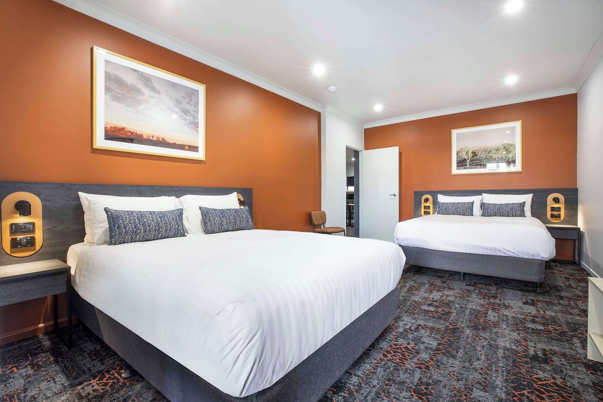 A hotel room with two beds, a large painting on the wall, and a carpeted floor.