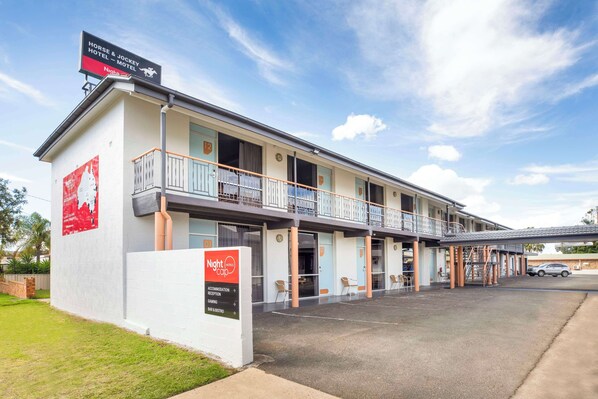 A motel with a balcony, a signboard, and a parking area.