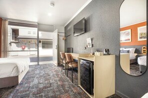 A hotel room with a bed, desk, chairs, a television, and a large mirror.