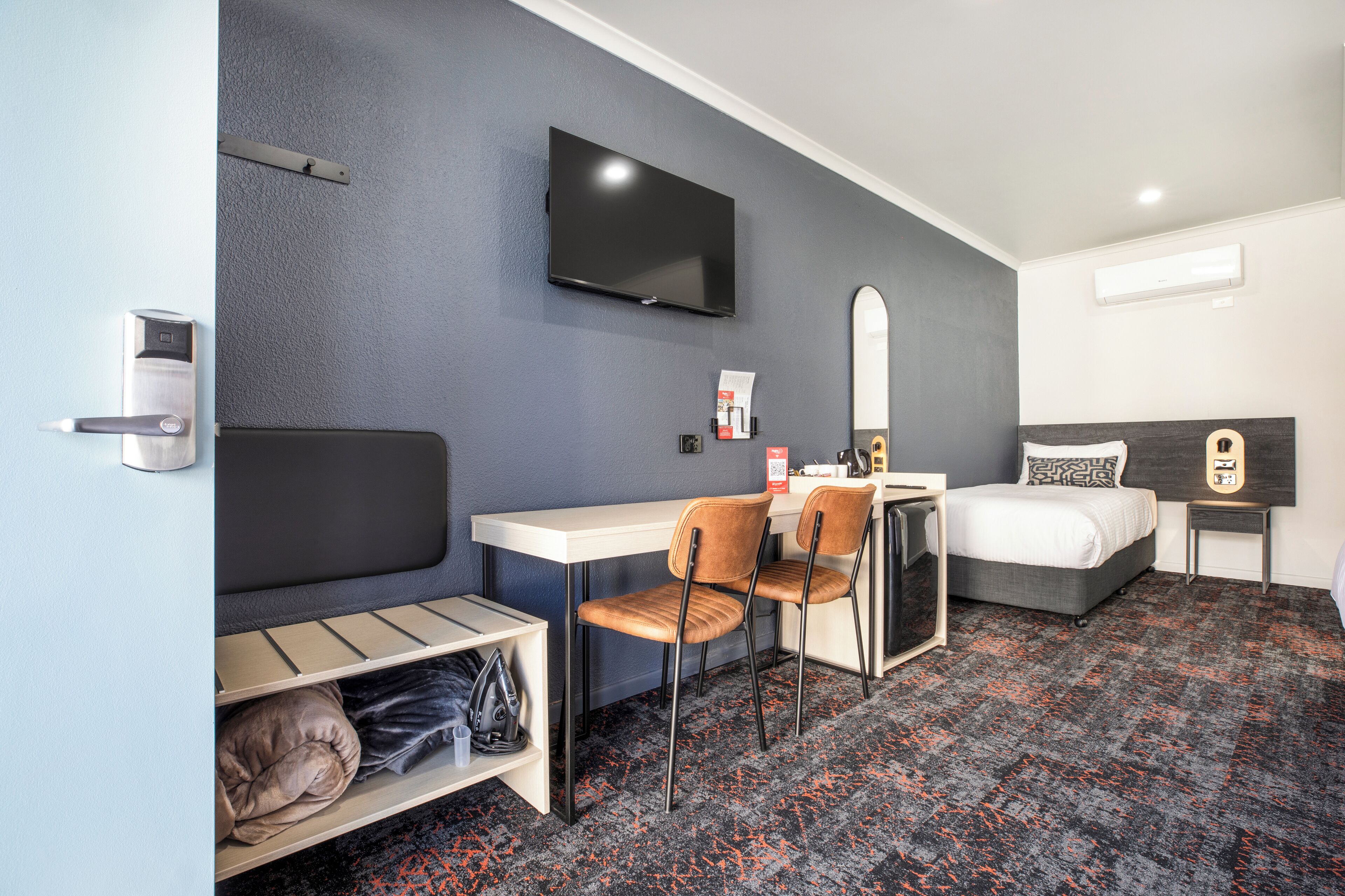 A hotel room with a bed, a desk, a chair, a TV, and a small table.