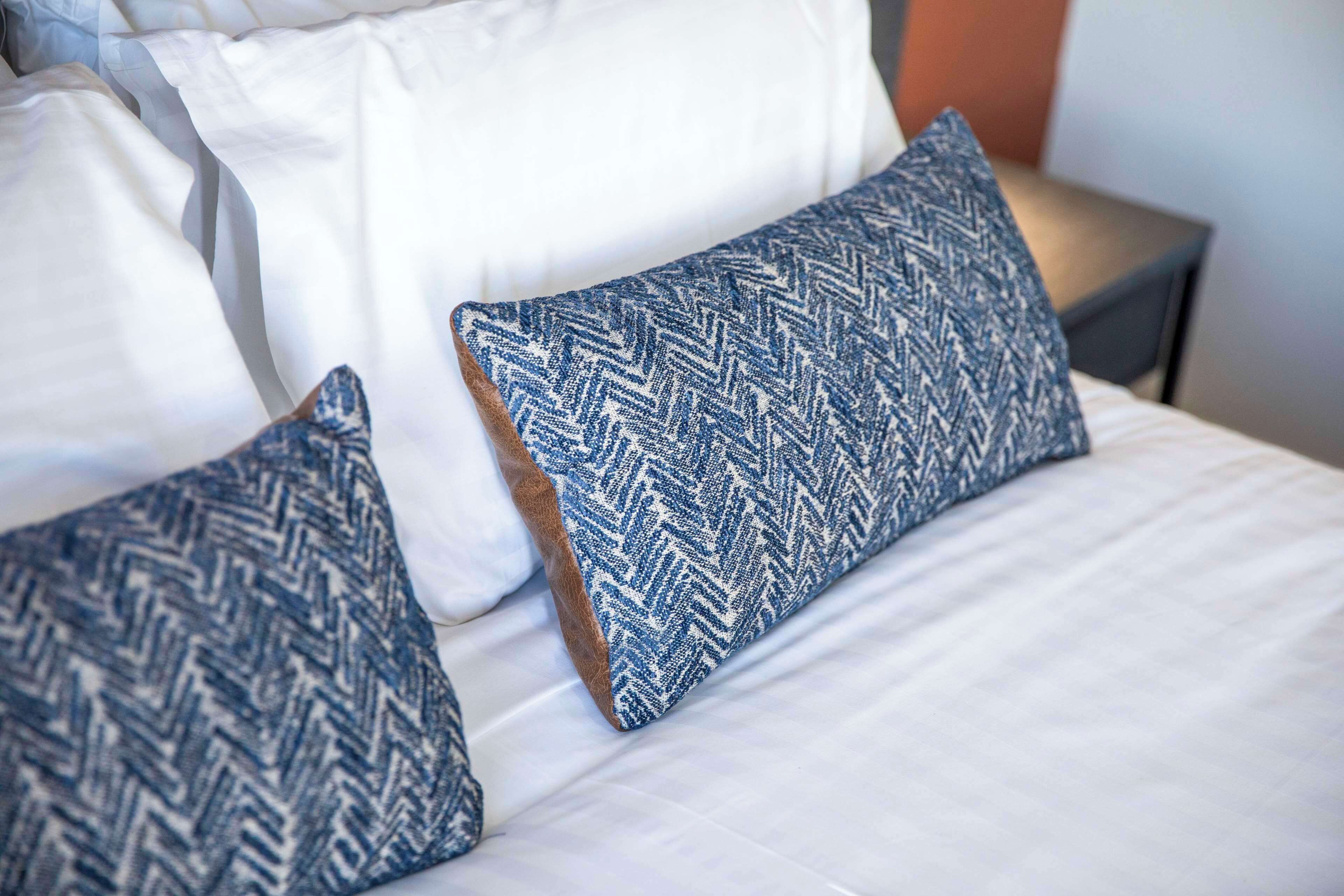 Een bed met witte beddengoed en twee blauw geblueseerde kussens.