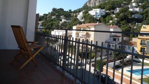 A balcony with a wooden chair, a view of a hillside with buildings, and a clear sky. - L Estartit: Apartment/ flat - L''ESTARTIT (L'ESTARTIT)