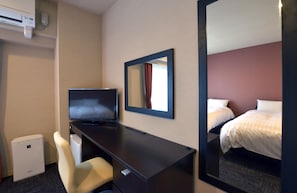 Een hotelkamer met een bed, een bureau met stoel, een televisie en een spiegel.