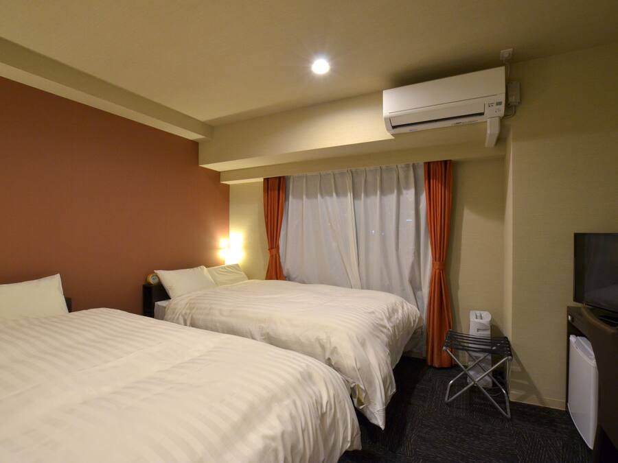 A hotel room with two beds, an air conditioning unit, a television, and a small table with a chair.