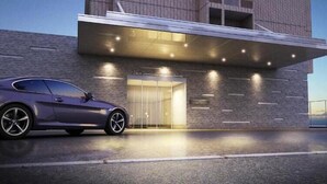 Un edificio moderno con entrada de vidrio y un coche estacionado frente a él.